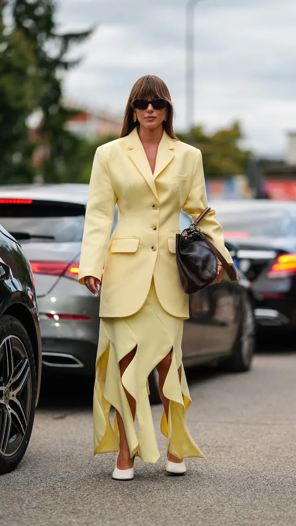 A woman wearing a butter yellow blazer and yellow midi skirt with a zig zag cutout outside Milan fashion week