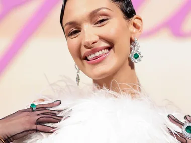 Bella Hadid in a white feathered top, sheer black gloves, showing off large diamond and emerald earrings and rings