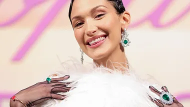 Bella Hadid in a white feathered top, sheer black gloves, showing off large diamond and emerald earrings and rings