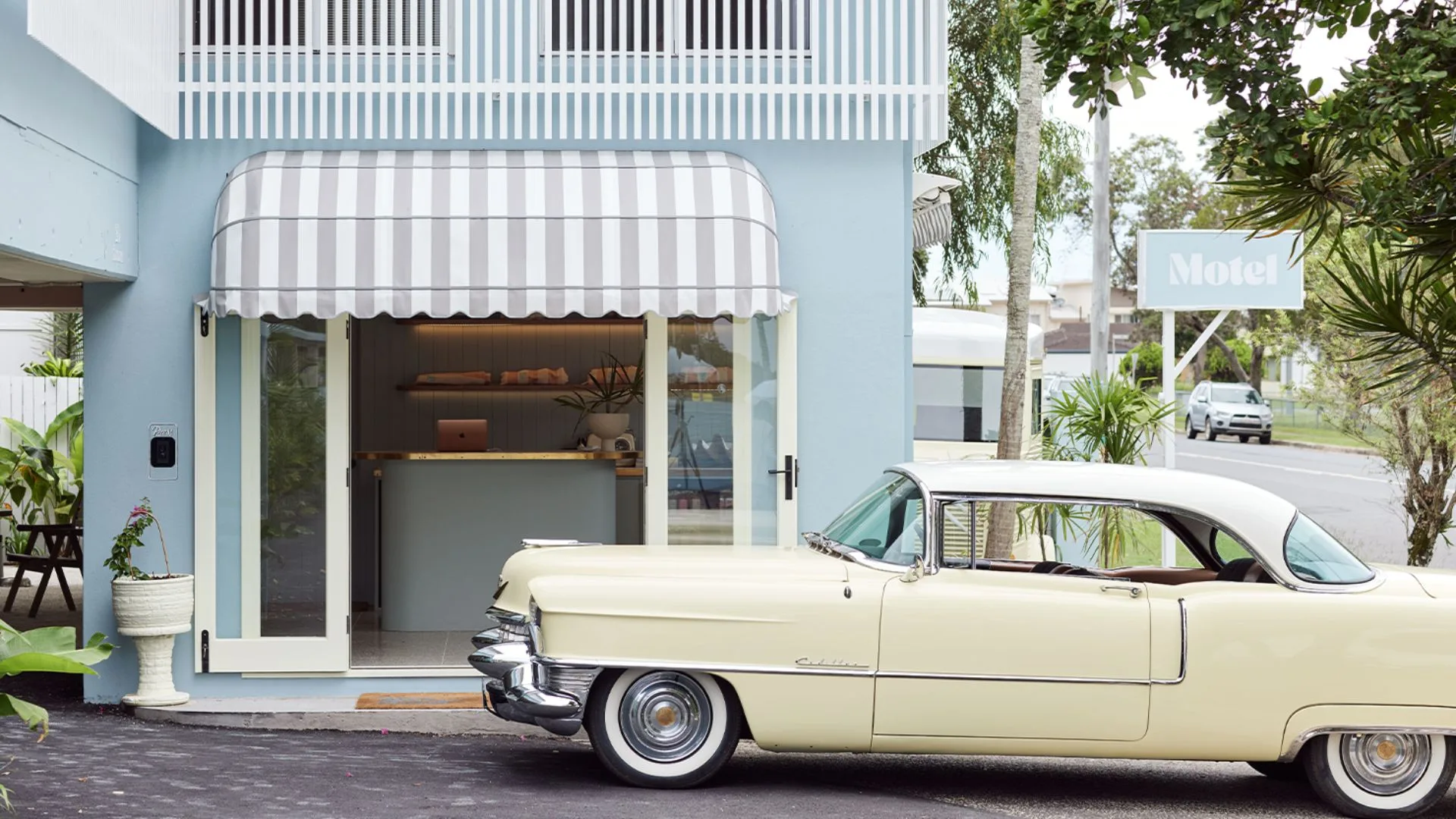 The retro exterior of the Blue Water Motel featuring a 1950s cream car parked out the front of the duck egg blue reception area. 