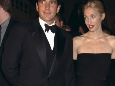 John F. Kennedy Jr. with his wife Carolyn Bessette Kennedy attending Municipal Art Society gala. Carolyn is wearing a black strapless midi dress and long black gloves. JFK is in a black tuxedo with a white shirt.