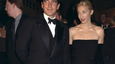 John F. Kennedy Jr. with his wife Carolyn Bessette Kennedy attending Municipal Art Society gala. Carolyn is wearing a black strapless midi dress and long black gloves. JFK is in a black tuxedo with a white shirt.