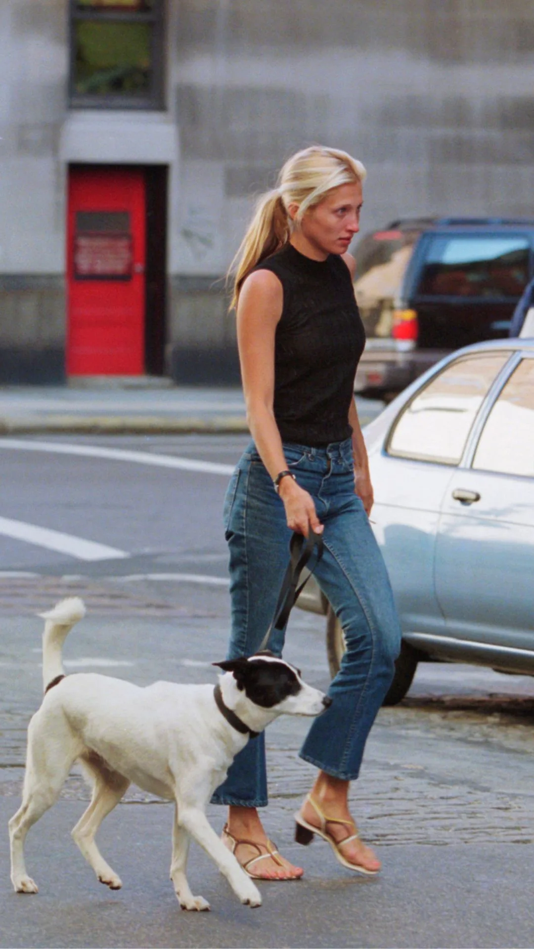 Carolyn Bessette Kennedy arrives home first walking their dog  in blue jeans and a black knit vest