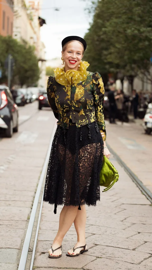 A woman dressed in a sheer lace black midi skirt and green and yellow