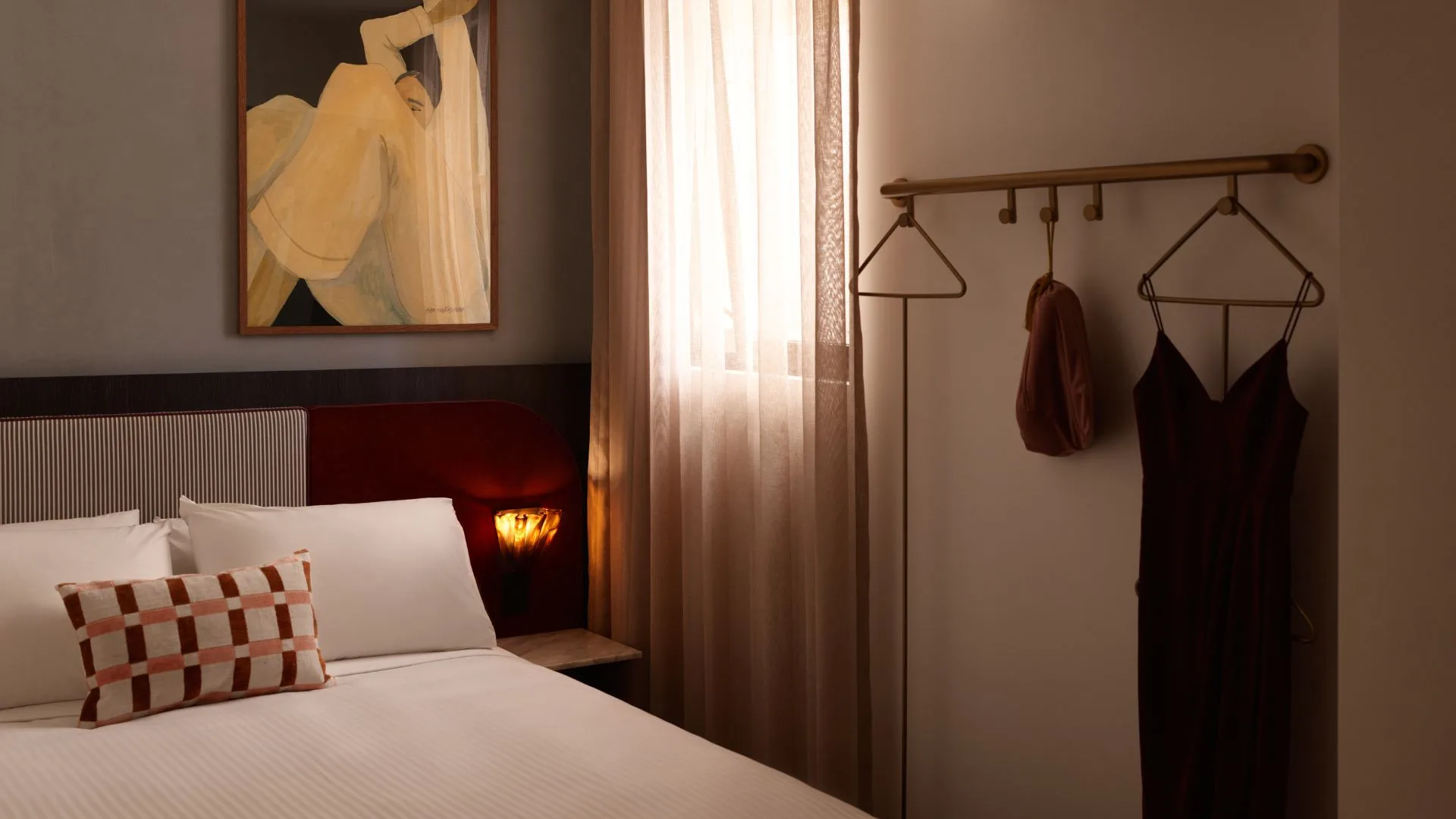 A picture of one of the suites at Hotel Morris in Sydney, The image shows a freshly made bed with white sheet, a red upholstered bedhead, blue wallpaper and a graphic artwork, with a clothes hanger in the background.