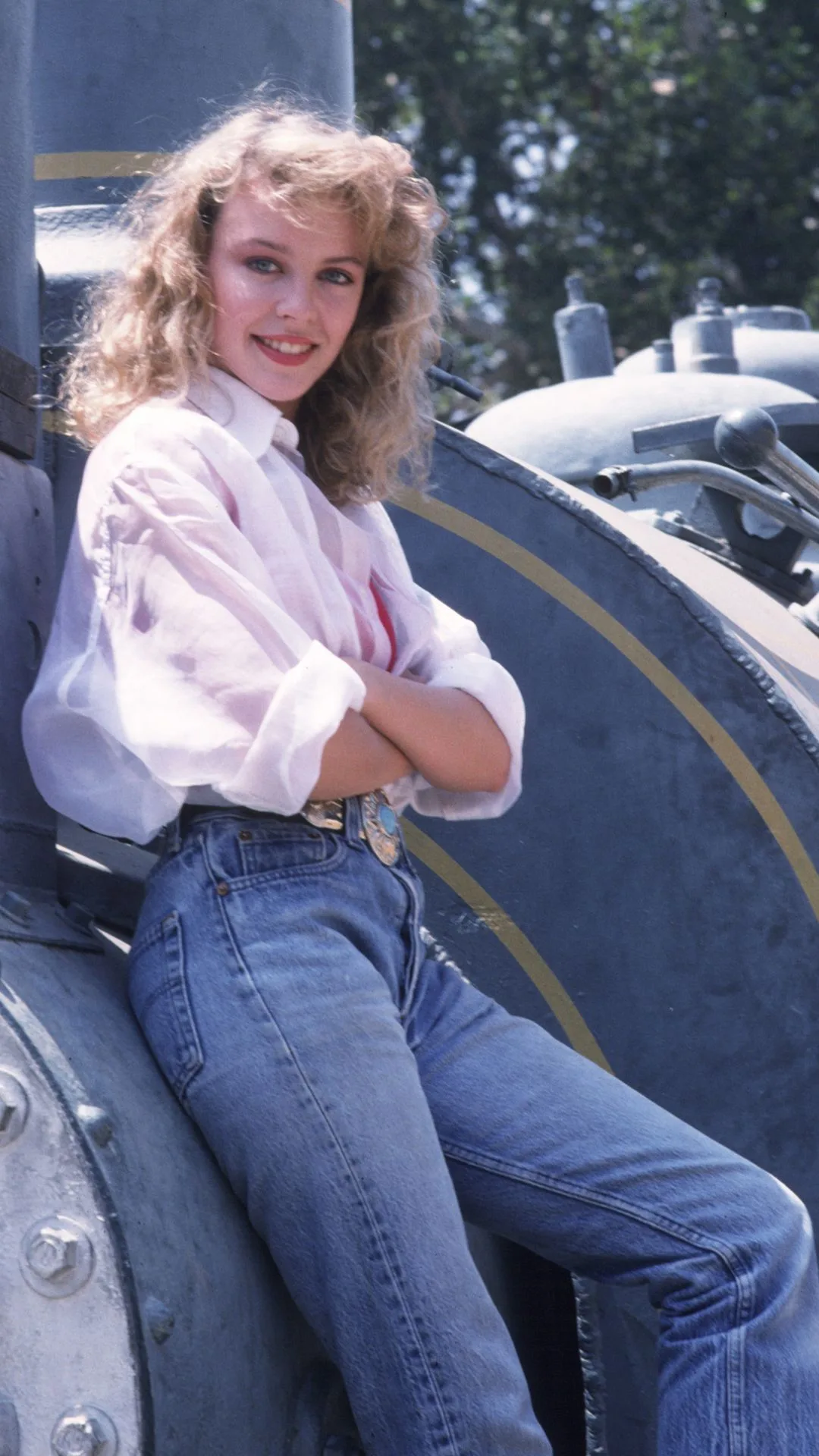 Kylie Minogue in 1988, posing on the side of an old steam train wearing blue jeans and a white shirt. 