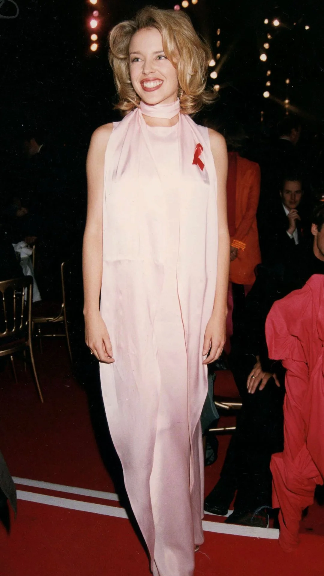 Kylie Minogue smiles on the red carpet at the 1997 BRIT awards wearing a long baby pink silk dress with matching silk scarf.