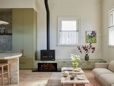 The sitting and kitchen area at Sona accommodation in Molong ,NSW. The green zellige tiled console runs along the back wall with a built in fireplace. A sage green kitchen with stone benchtop is seen on the far left corner.