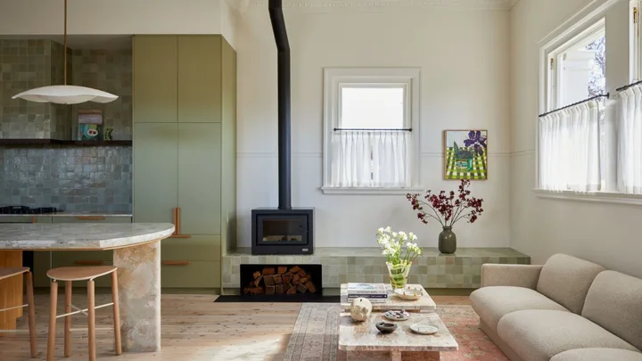 The sitting and kitchen area at Sona accommodation in Molong ,NSW. The green zellige tiled console runs along the back wall with a built in fireplace. A sage green kitchen with stone benchtop is seen on the far left corner.