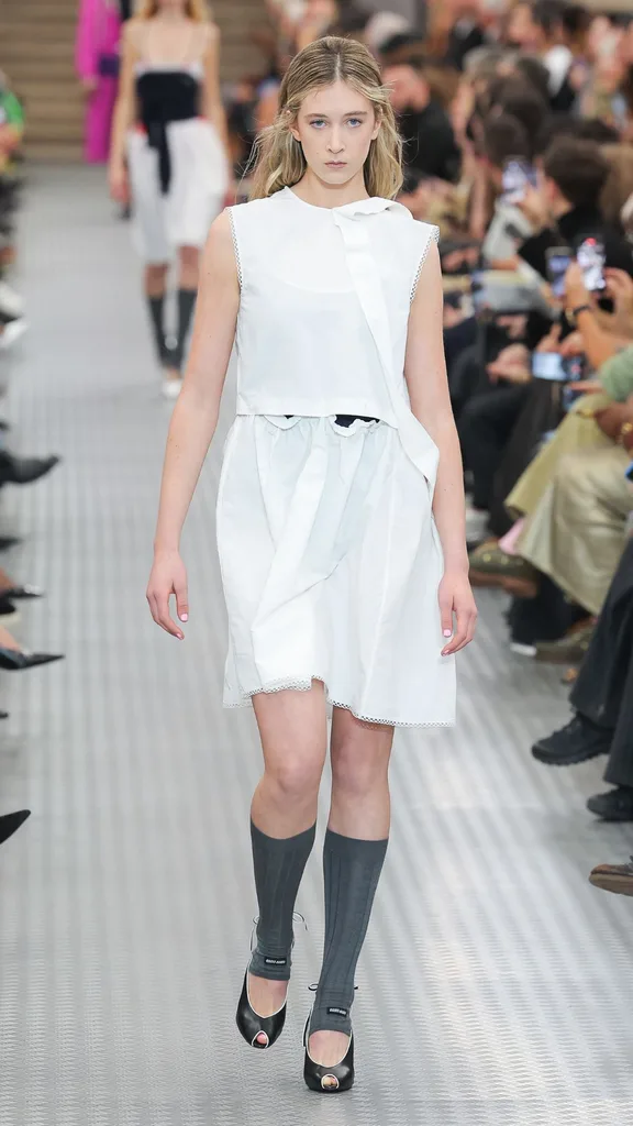 Sunday Rose walks the runway during the Miu Miu Paris Womenswear Spring-Summer 2025 show wearing a white dress.
