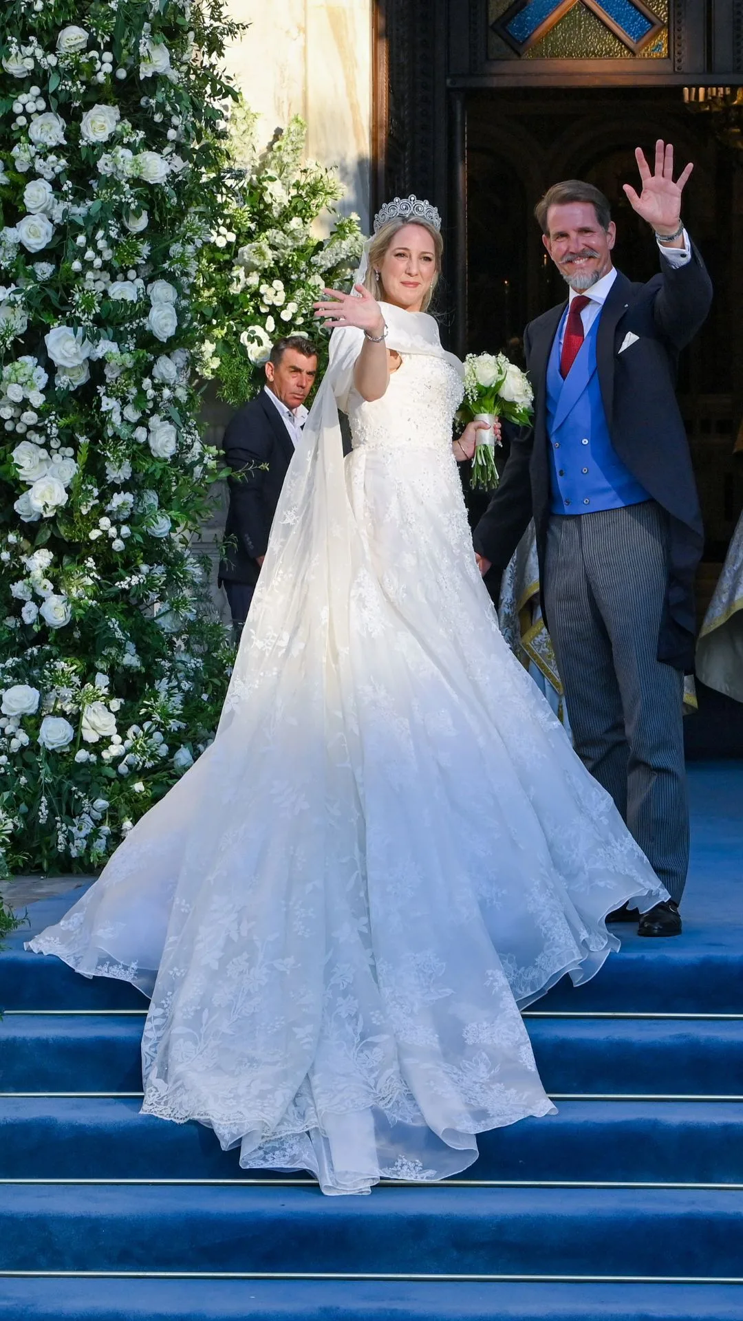 Theodora of Greece arrives on the arm of her brother Paul, who wears a pinstripe suit with dark blue vest.