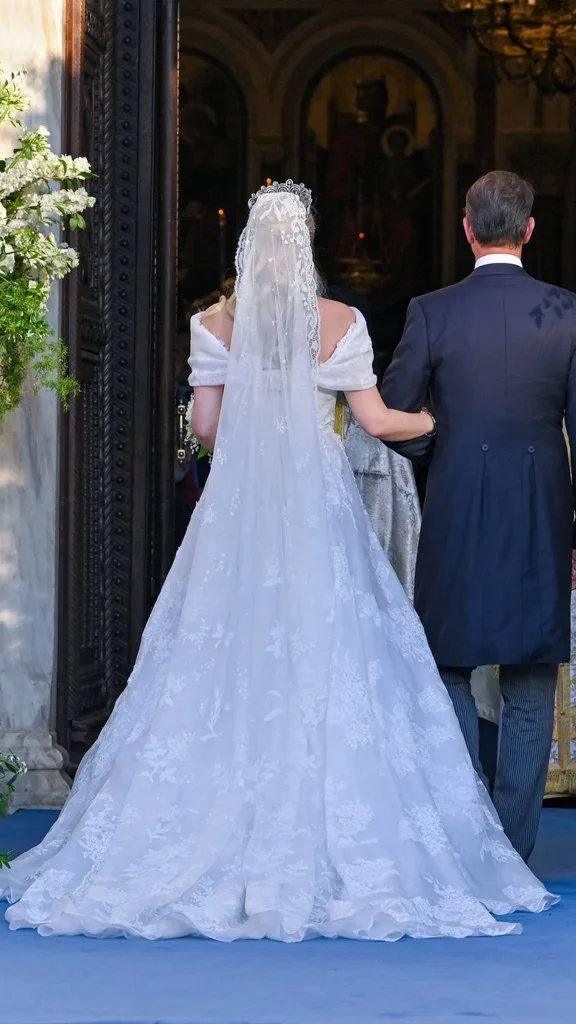 Theodora of Greece arrives on the arm of her brother Pavlos, Crown Prince of Greece, to her wedding at the Metropolis Greek Orthodox Cathedral. The bride wore a traditional white embroidered wedding dress with long white veil.