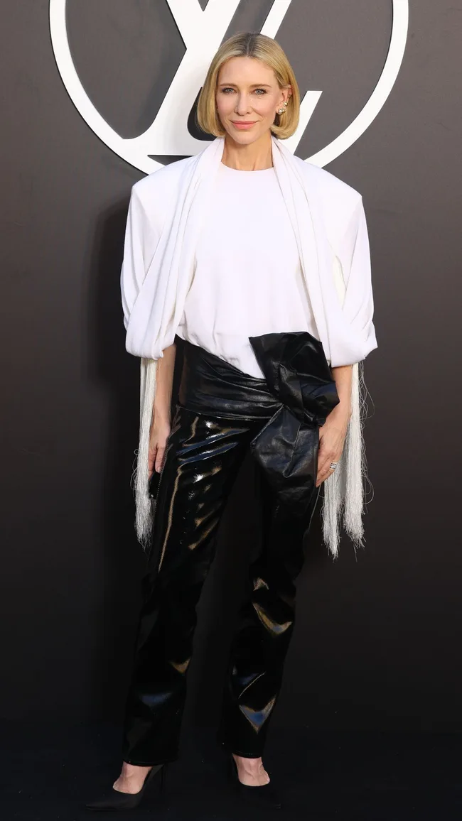 Cate Blanchett attends the Louis Vuitton Paris Womenswear Spring-Summer 2025 show wearing a white sculptural shirt and black patent leather pants with an oversized black bow belt.