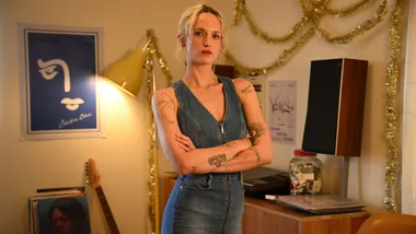 A still image from the new adaptation of Paul Kelly's song 'How To Make Gravy' showing character Rita standing in a living room.