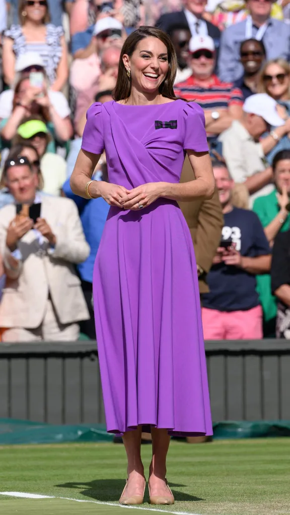 Catherine, Princess of Wales on court to present the trophy to the winner of the men's final on day fourteen of the Wimbledon Tennis Championships at the All England Lawn Tennis and Croquet Club on July 14, 2024. The princess wears a purple short sleeved midi dress with nude coloured high heels.