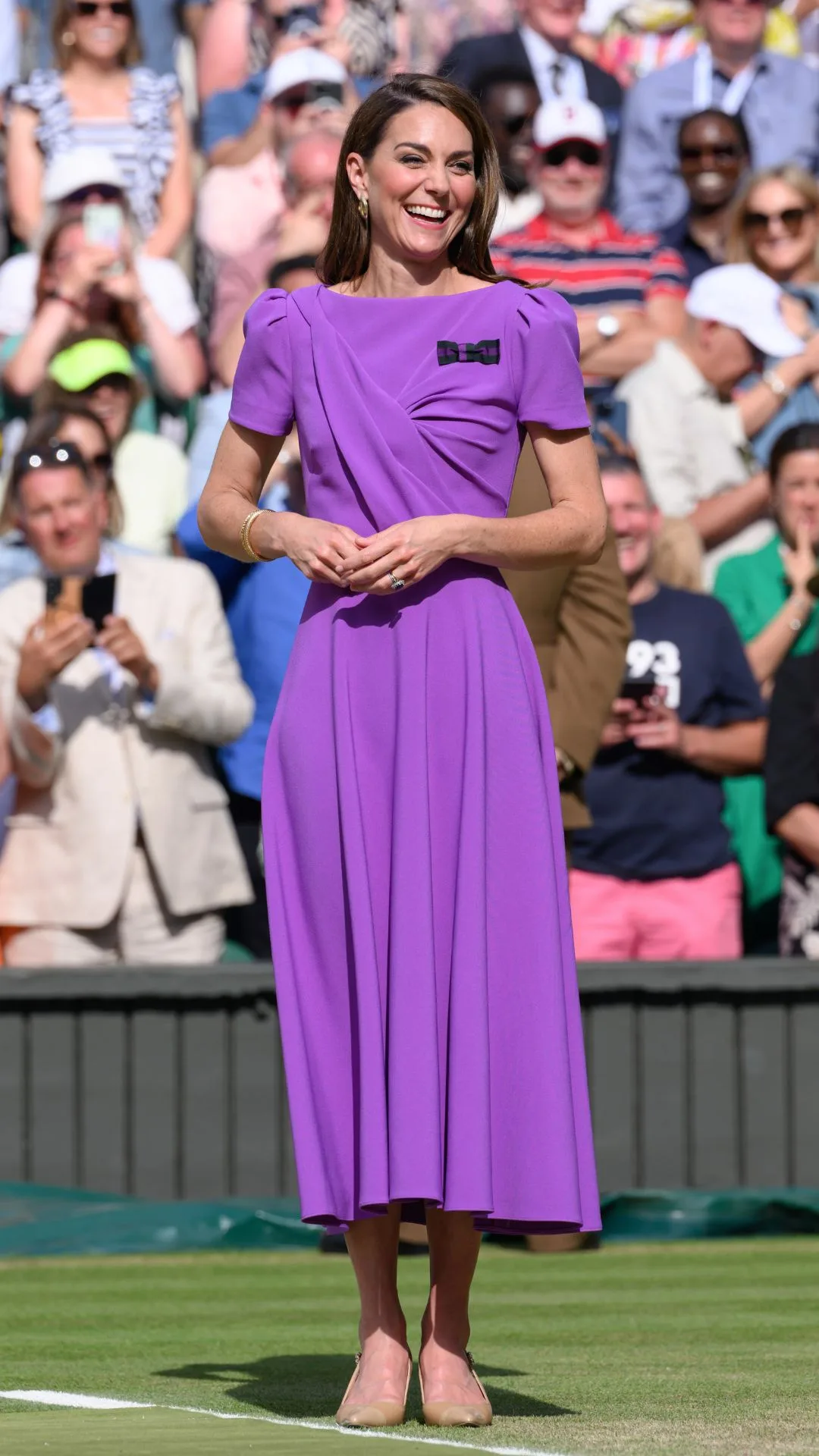 Catherine, Princess of Wales on court to present the trophy to the winner of the men's final on day fourteen of the Wimbledon Tennis Championships at the All England Lawn Tennis and Croquet Club on July 14, 2024. The princess wears a purple short sleeved midi dress with nude coloured high heels. 