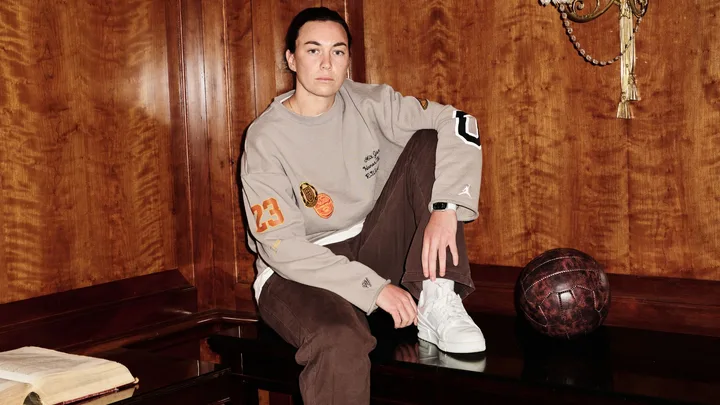 Goalkeeper for the Matildas, Mackenzie Arnold poses for a portrait in a wooden panelled room sitting on a mahogany bench a beige and brown tracksuit ahead of The Best FIFA Football Awards 2023