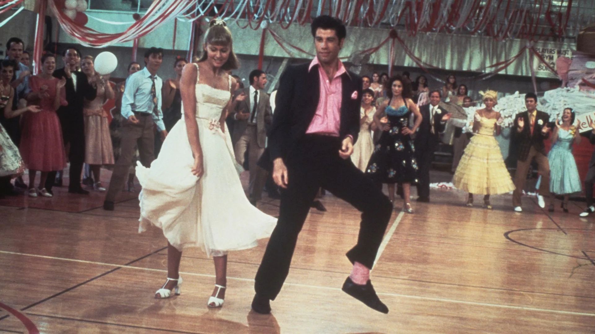 Olivia Newton-John and American actor John Travolta dance in a crowded high school gym in a still from the Paramount film, 'Grease', 1978