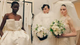 Backstage at Richard Quinn RTW Spring 2025 as part of London Ready to Wear Fashion Week held at The Dorchester Hotel Park Lane. The picture shows three models wearing white gowns with features, lace and beading holding wedding-like bouquets.