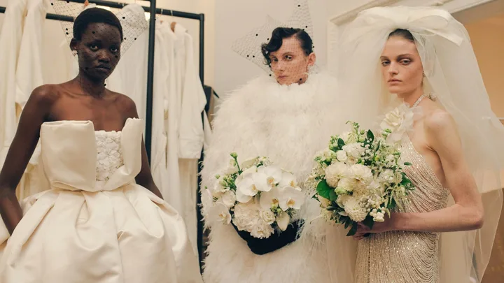 Backstage at Richard Quinn RTW Spring 2025 as part of London Ready to Wear Fashion Week held at The Dorchester Hotel Park Lane. The picture shows three models wearing white gowns with features, lace and beading holding wedding-like bouquets.