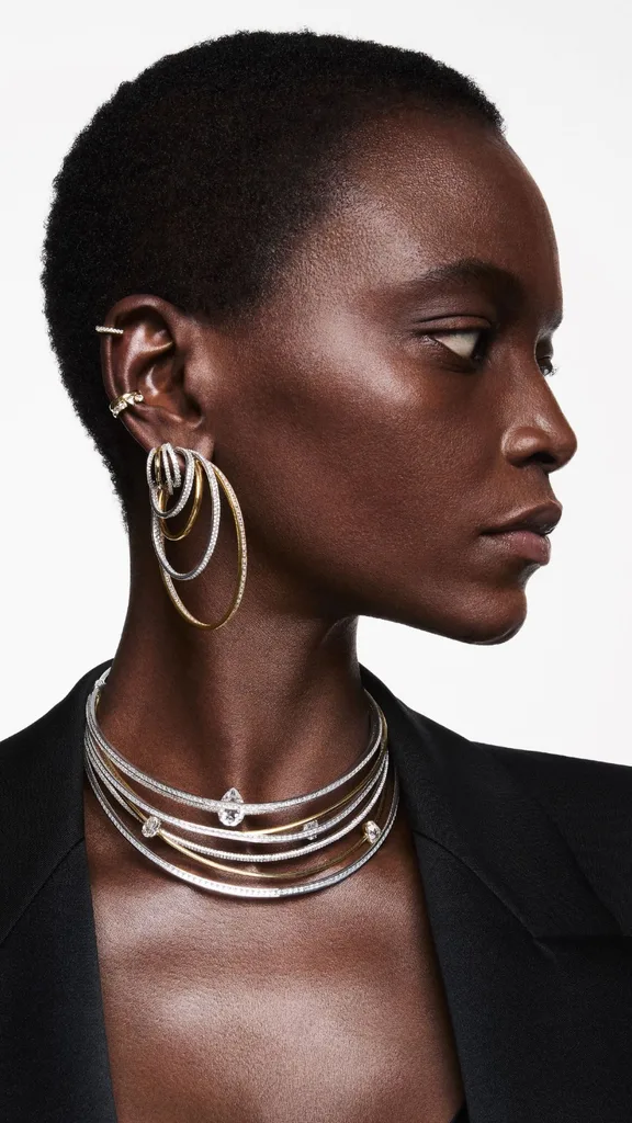 A woman modelling hoop-style stacked earrings and necklaces in silver and gold from the Swarovski Fall/Winter 2024 jewellery collection.