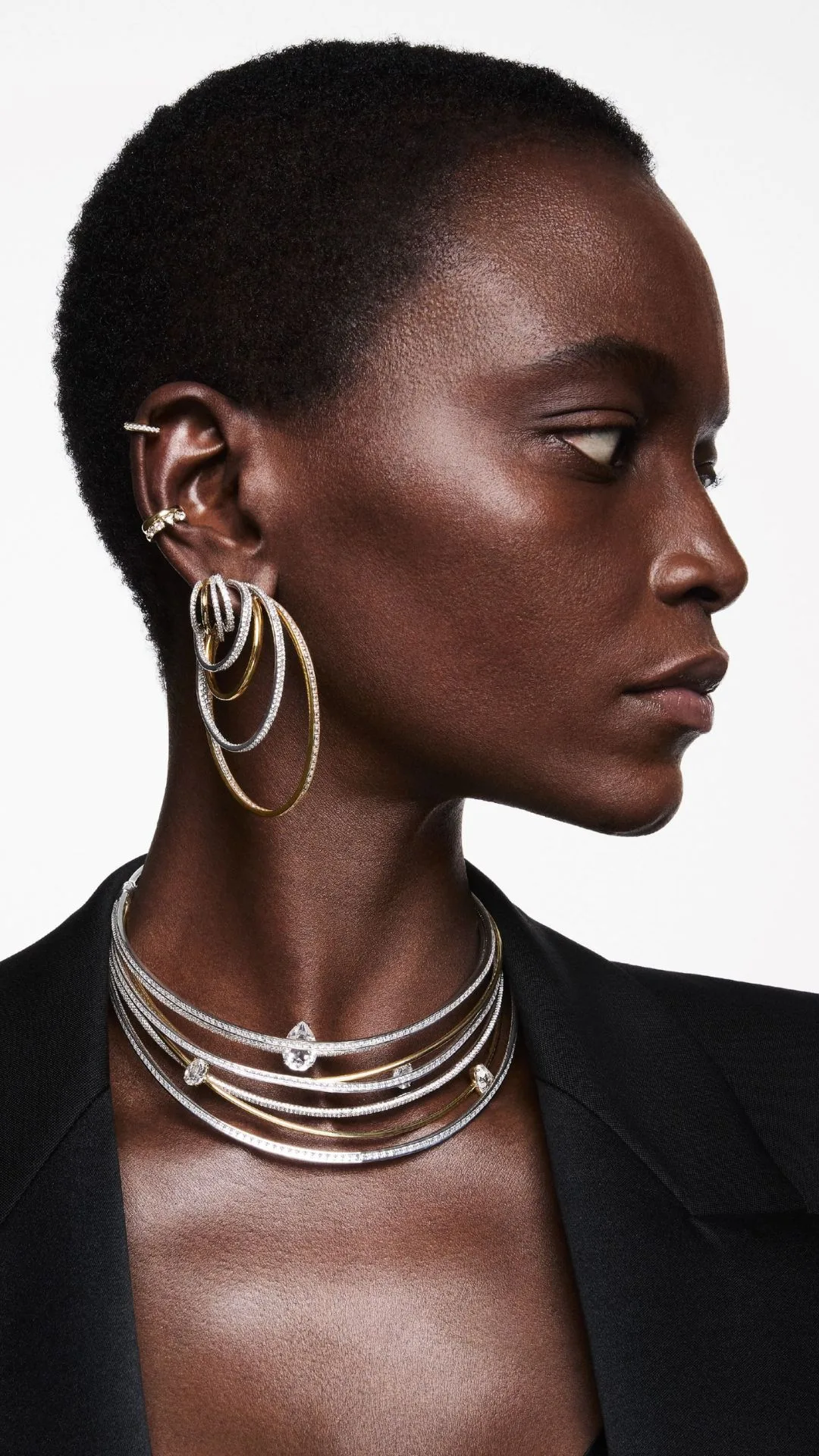 A woman modelling hoop-style stacked earrings and necklaces in silver and gold from the Swarovski Fall/Winter 2024 jewellery collection. 