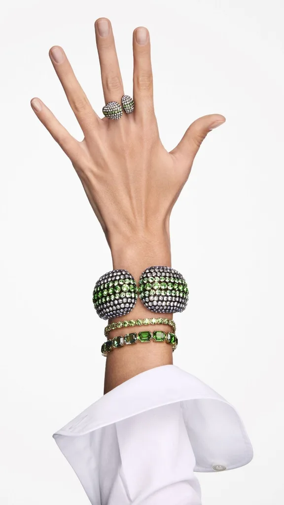 A woman's hand is pictured modelling pieces from the Swarovski Fall/Winter 2024 collection including bold geometric green bangles, pave bracelets and a matching green green crystal pave ring.