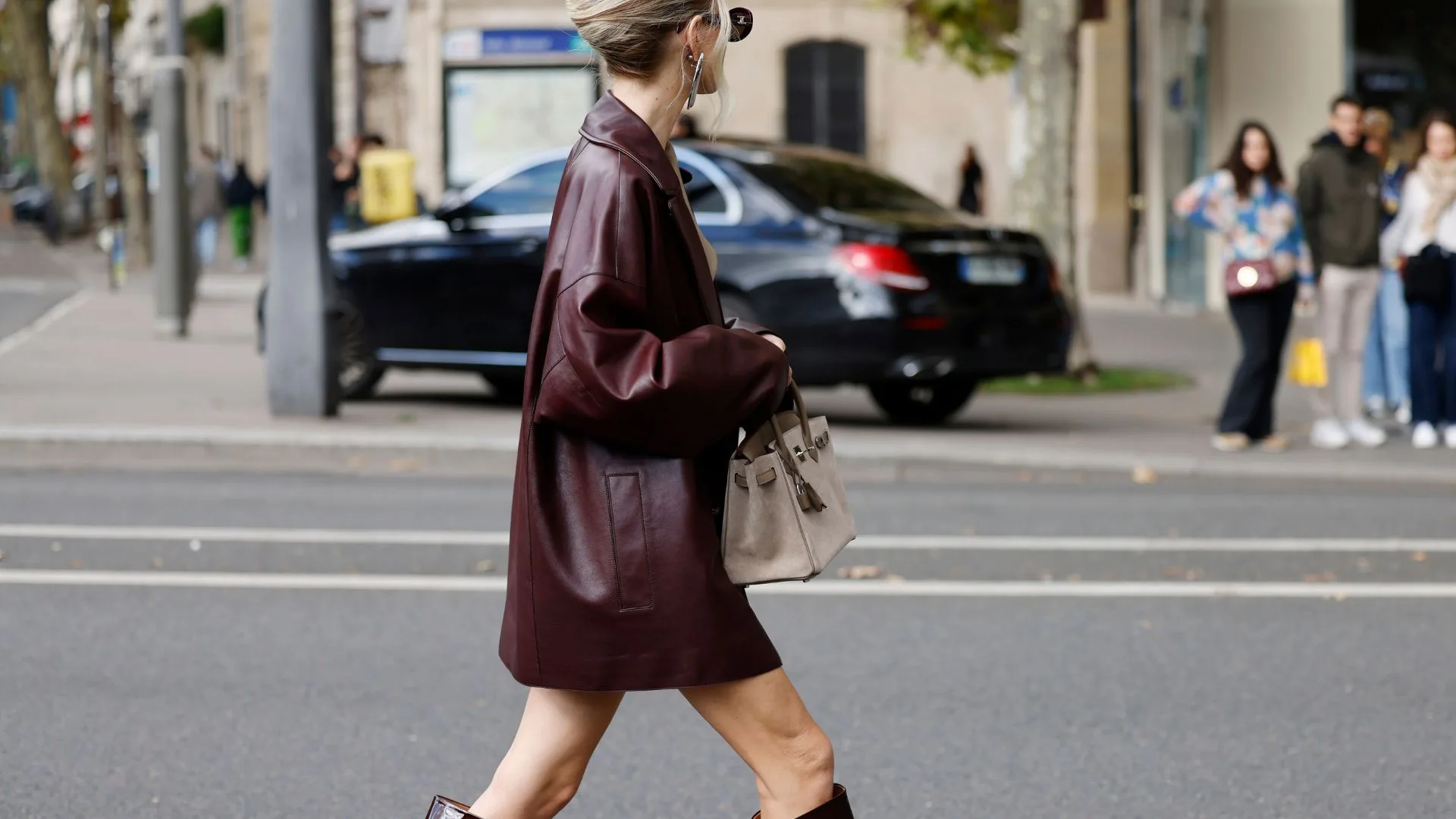 Leonie Hanne wears beige shirt with matching shorts, burgundy leather blazer, burgundy boots, beige Hermes suade bag, outside Hermes