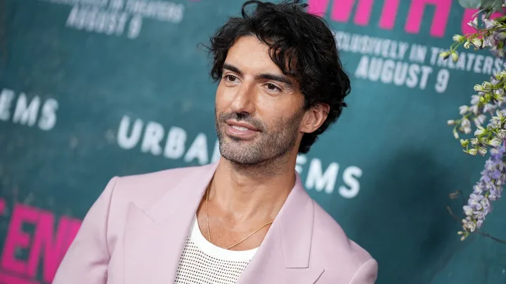 A man wearing a pink suit and white t shirt smiling.