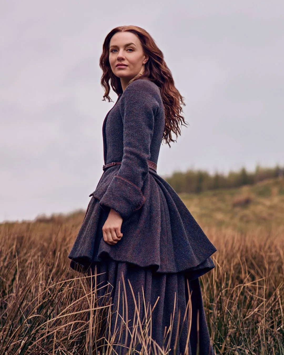 A woman with red hair standing in a field. 