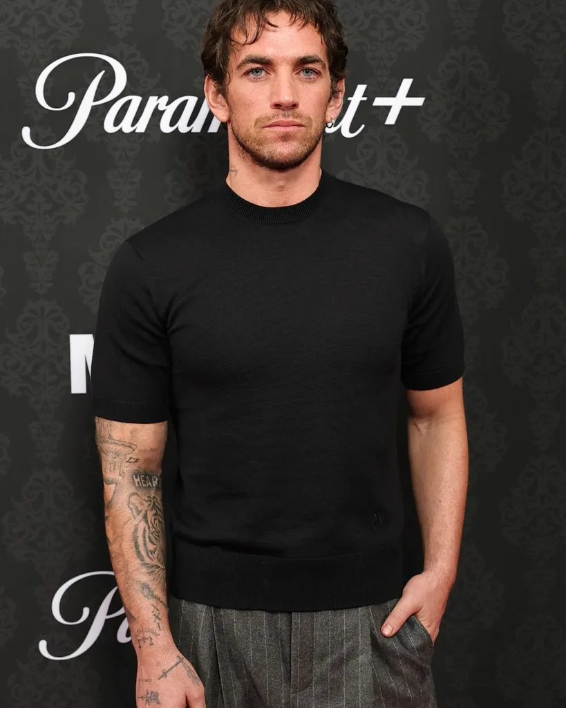 Actor Alex Fine wearing a black t shirt and grey pants on the red carpet.