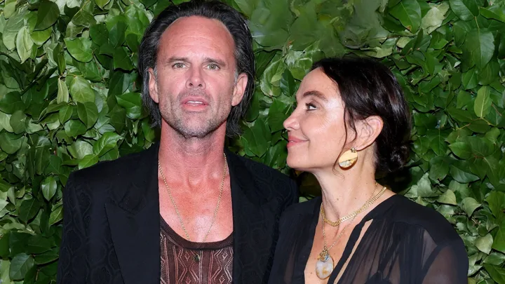 Walton Goggins and his wife Nadia in front of a wall covered in green leaves.