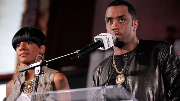 Dawn Richards and P Diddy standing in front of a microphone at a press conference in 2010.
