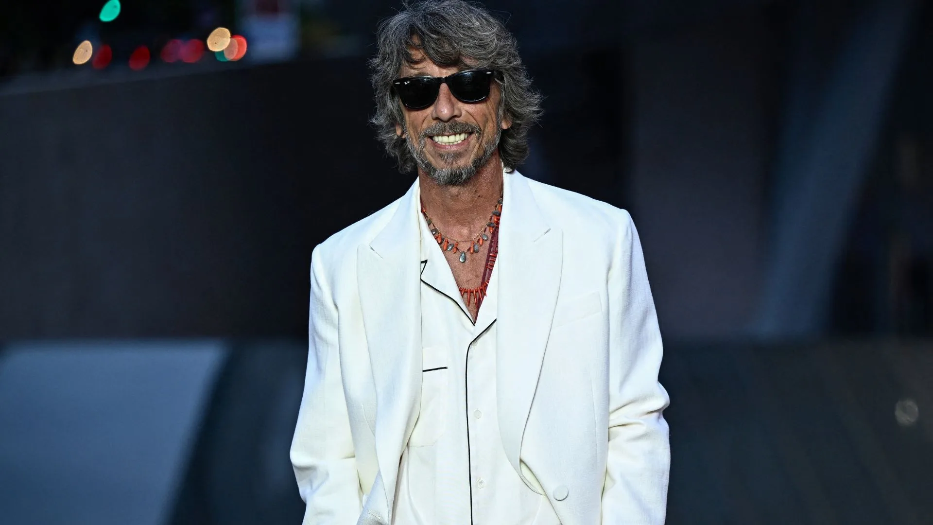 Designer Pier Paolopicari sourit avec un costume blanc et des lunettes de soleil noires 