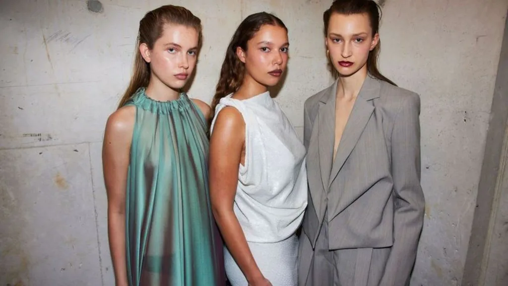Three models standing in front of a grey concrete wall