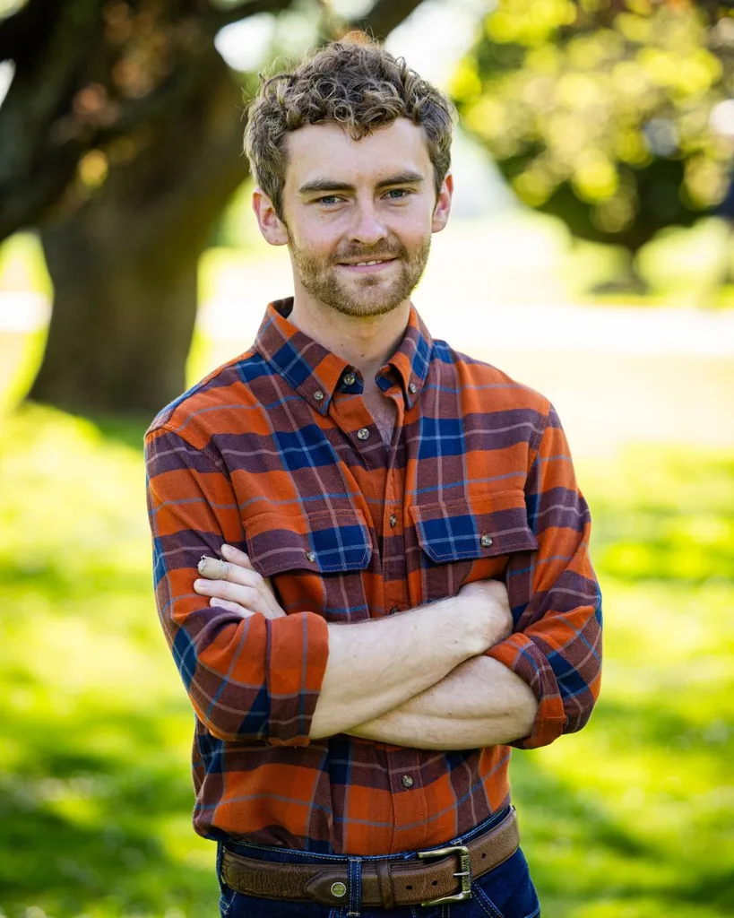 A man wearing an orange and blue plaid shirt crossing his arms.