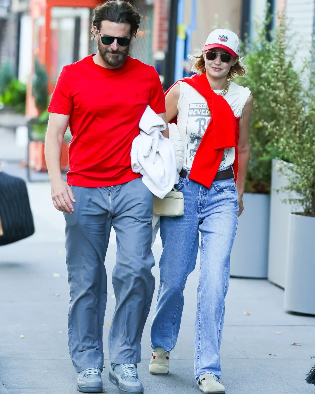 Bradley Cooper and Gigi Hadid walking on the streets of New York City dressed in matching blue jeans and white and red tops. 