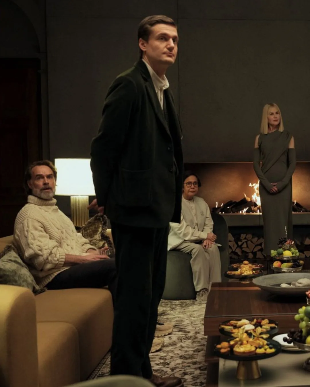 A group of people sitting in a living room in front of a fireplace. 