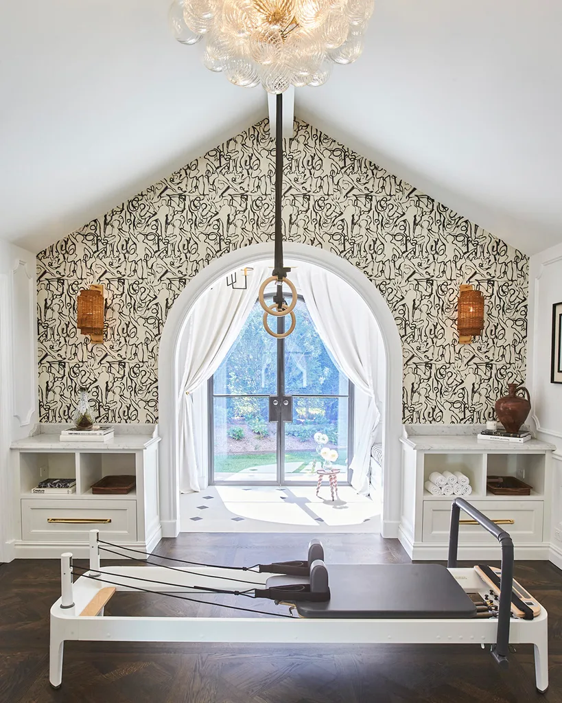 The gym at Romney House. A room with a white pitched roof. One wall is covered with patterned wallpaper and there's a pilates reformer machine in the centre of the room.
