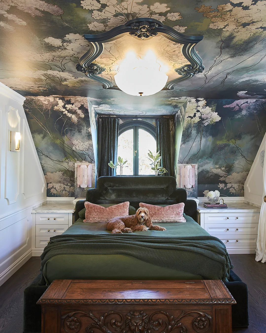 A bedroom with a bed laid with dark green linen. The roof is pitched and covered in garden-motif wallpaper. 