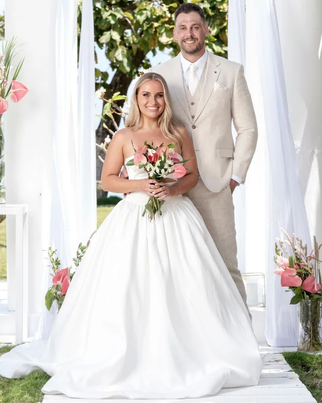 A man and woman dressed in wedding attire standing and smiling on a beach.