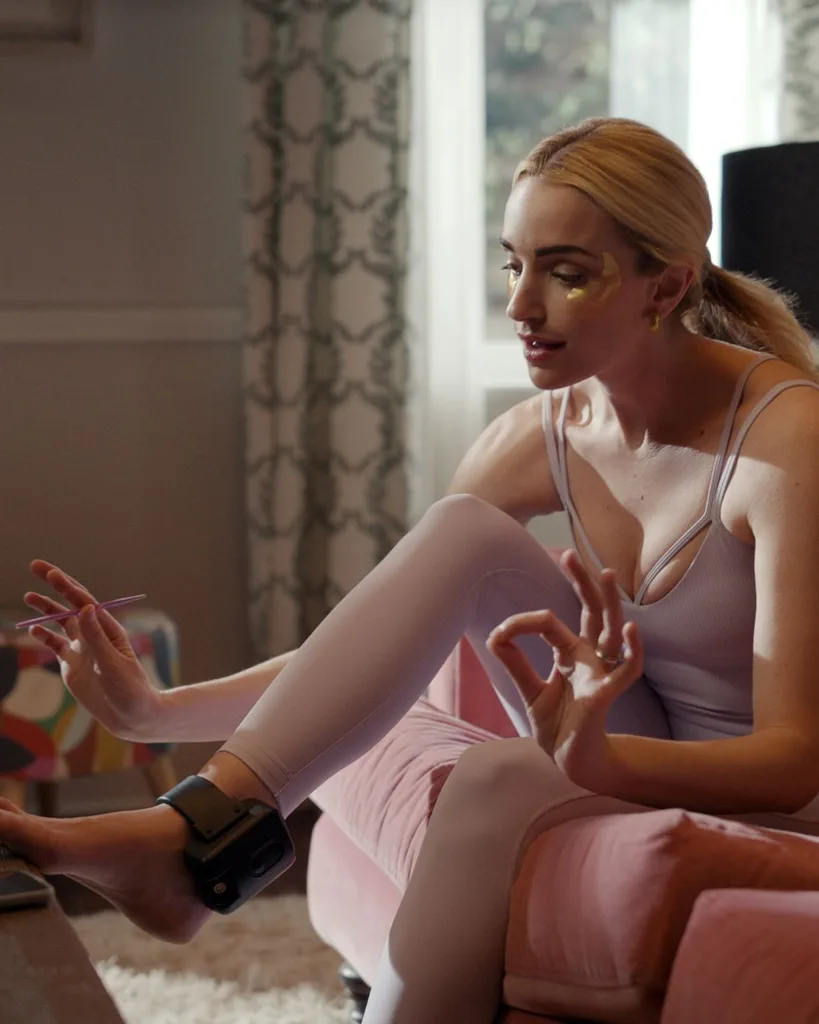 A woman wearing an ankle monitor and pink workout clothes painting her toenails.