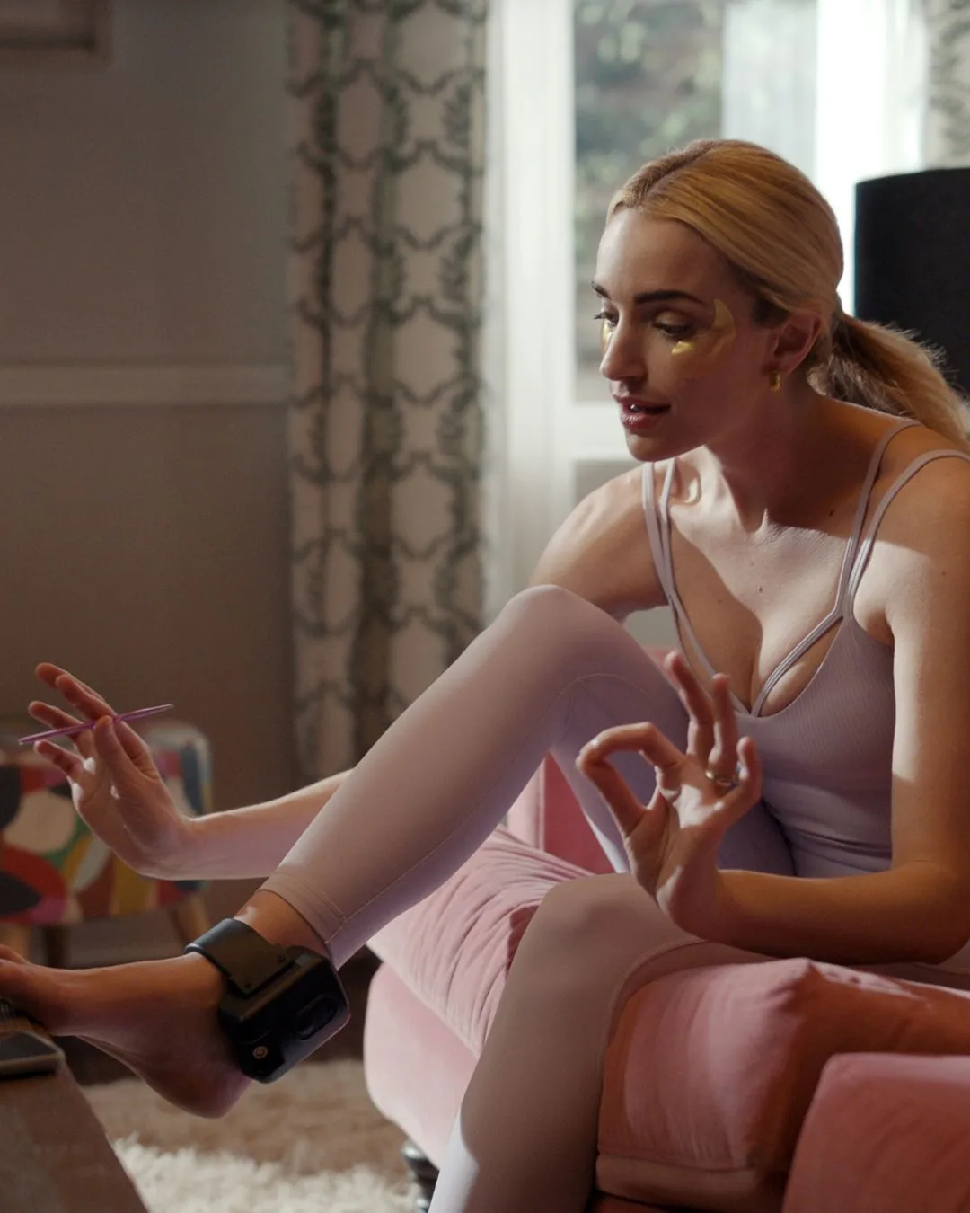 A woman wearing an ankle monitor and pink workout clothes painting her toenails.