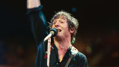 A still image of a man singing in front of a microphone