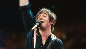 A still image of a man singing in front of a microphone