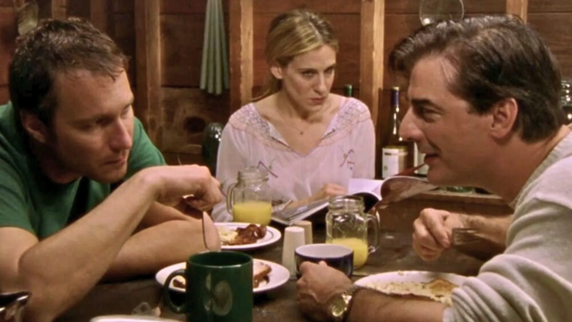 A woman looking concerned as two men talk to each other across the table. 