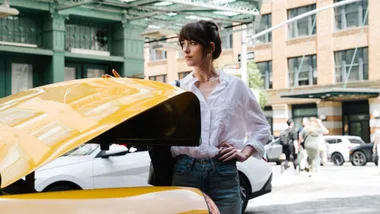 A woman wearing a white shirt and blue jeans waiting at the back of a taxi