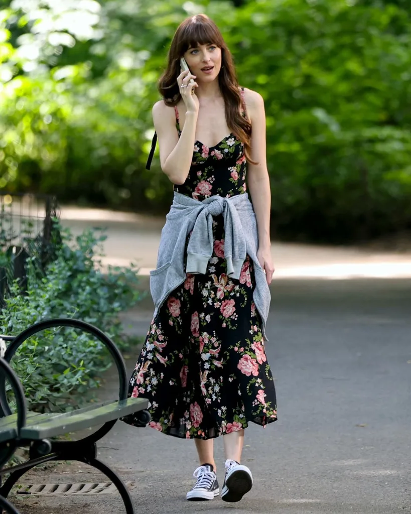 A woman holding her phone to her ear walking in the park in a floral dress.