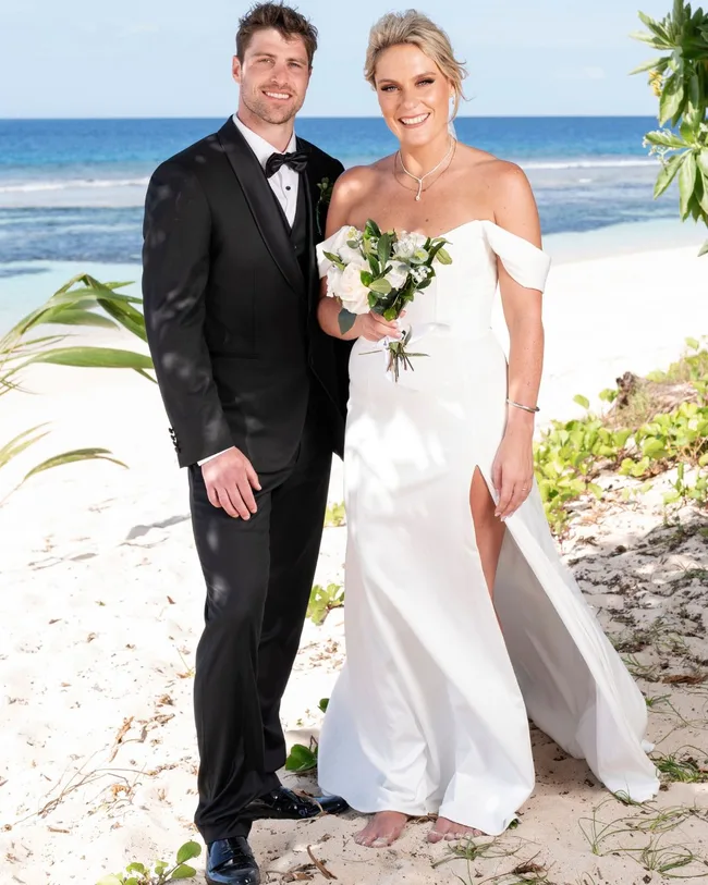 A man and woman dressed in wedding attire standing and smiling on a beach.