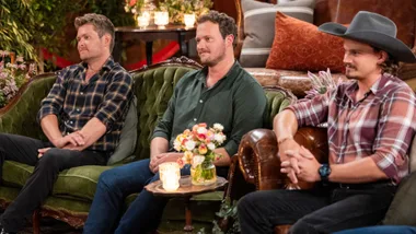 Three men dressed in shirts and jeans sitting on a couch.